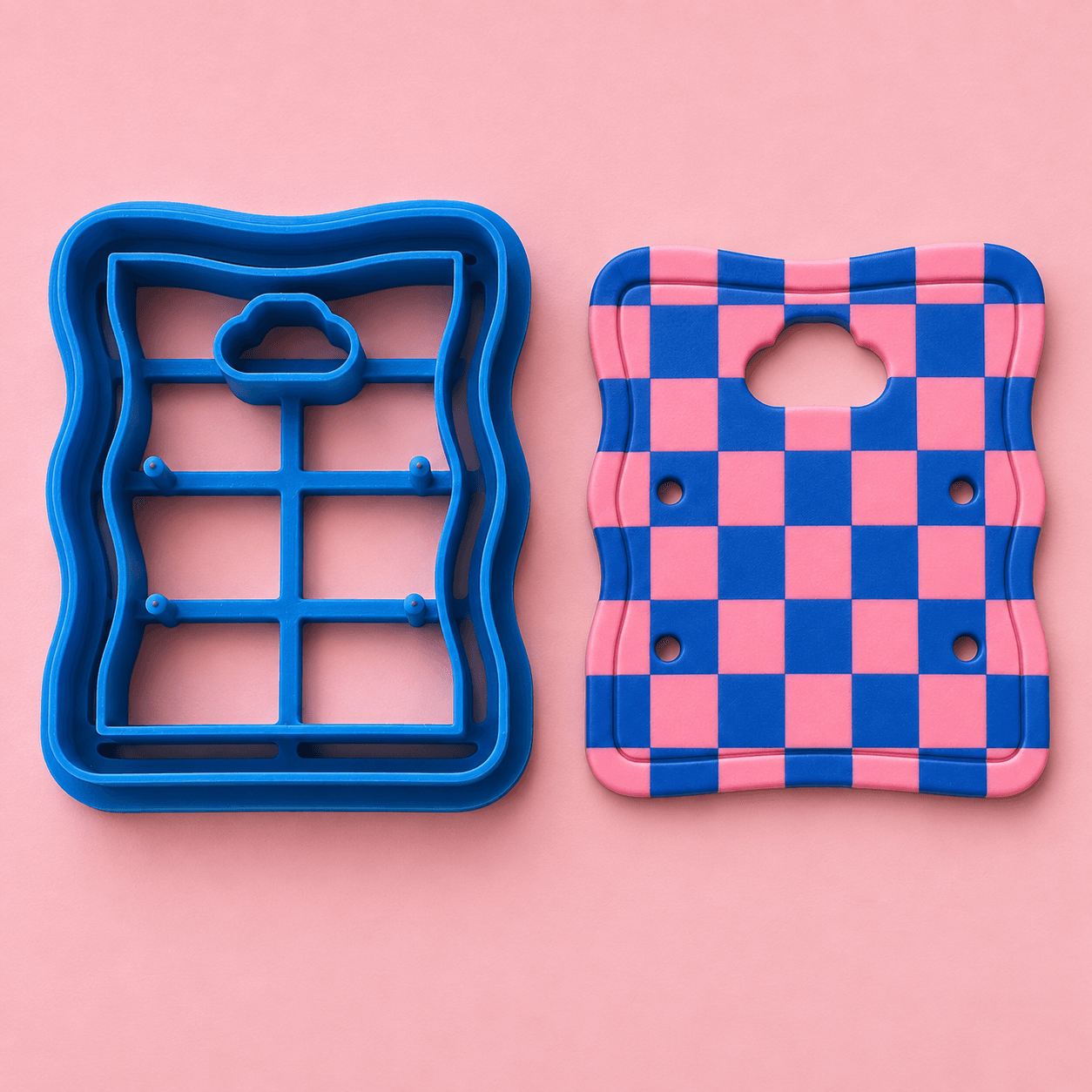 A blue 3D-printed card cutter beside a pink and blue checkerboard clay card cut with it.