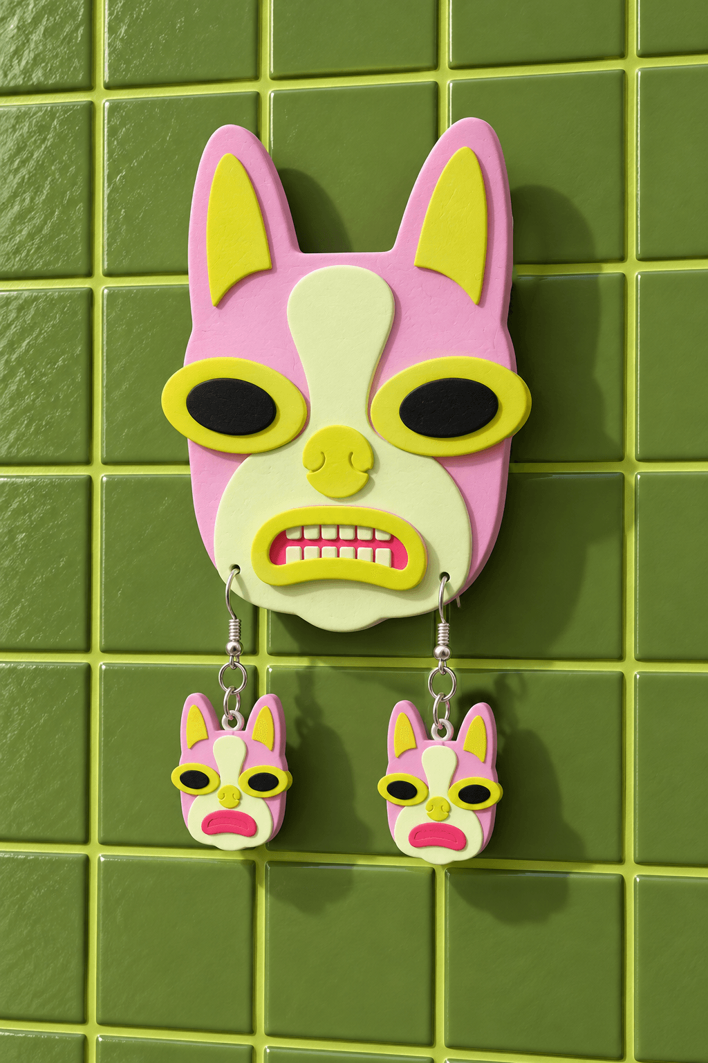 Pink and yellow Boston Terrier wall display holding two matching drop earrings against olive tiles.