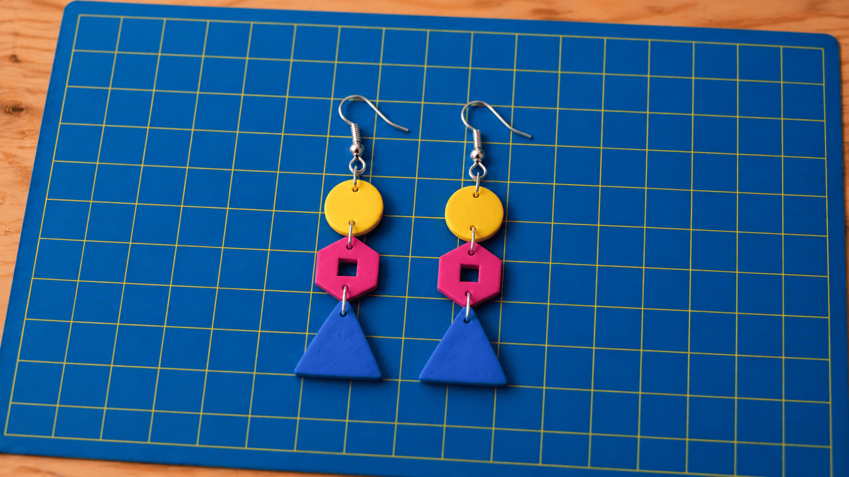 A shorter Go-Go dangle earring: a yellow disc, one hex link and a blue triangle on an ear wire.